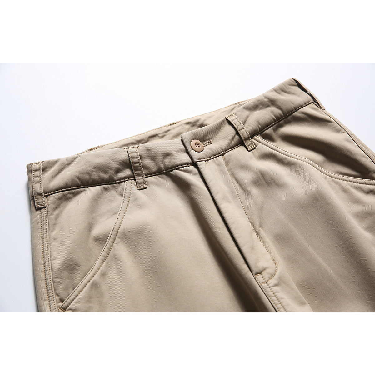 Close-up of beige trousers showing the waistband, button, belt loops, fly, and curved front pocket.