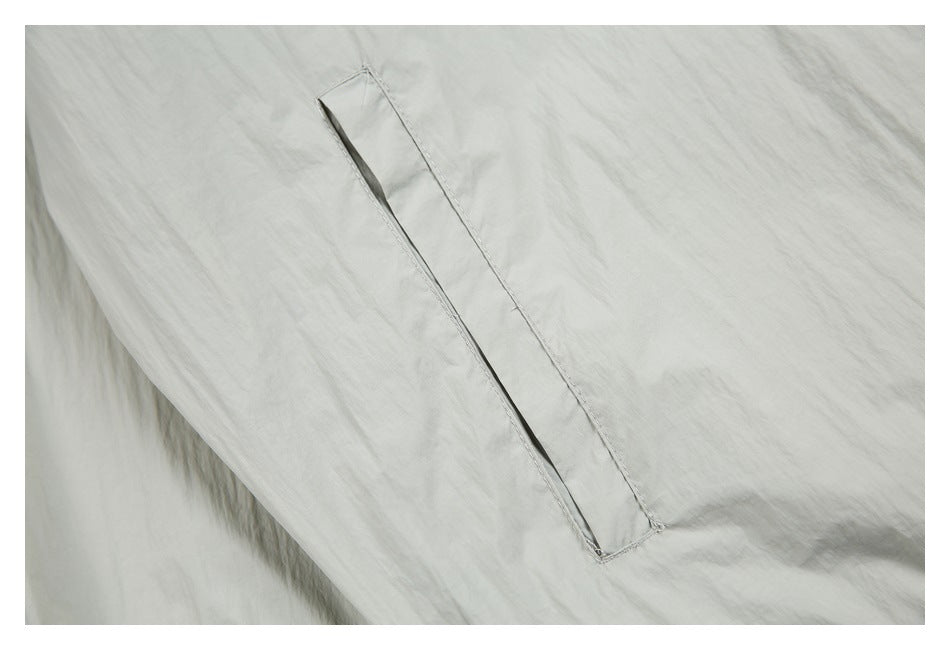 Close-up of a narrow angled welt pocket on light gray windbreaker fabric.