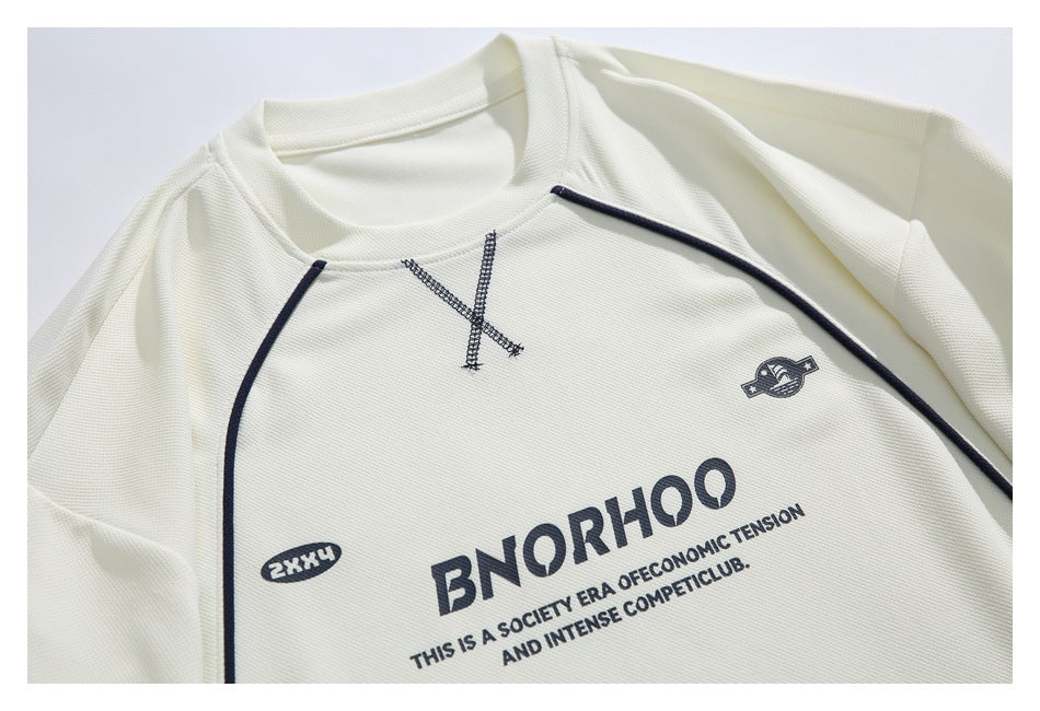Close-up of the off-white T-shirt's chest, with dark piping, a stitched X, small emblems, and English print.