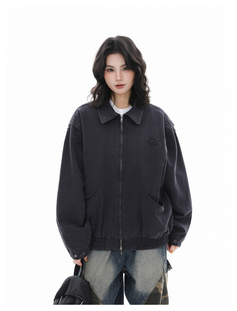 Model in an oversized charcoal gray zip jacket with a pointed collar and front pockets, faded camo-panel jeans