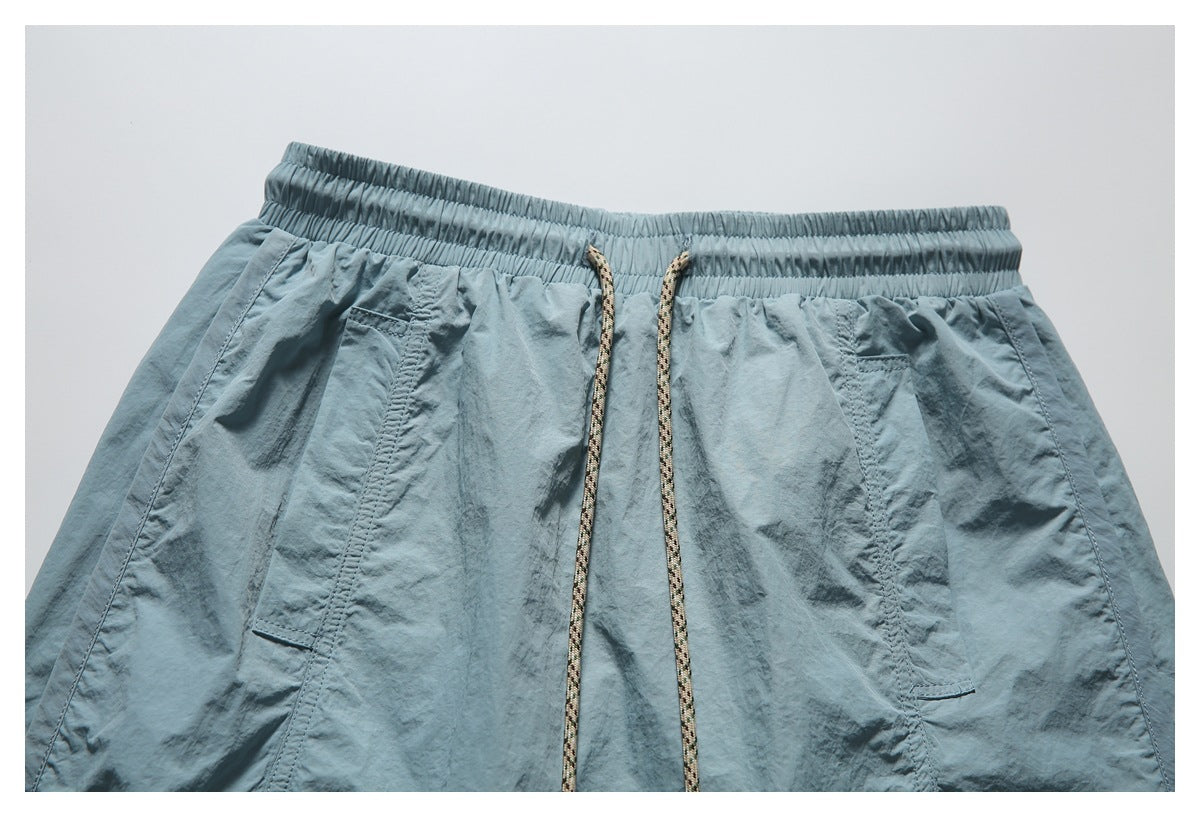 Close view of the front of blue-gray shorts with an elastic waistband, patterned drawstring, and angled pockets.