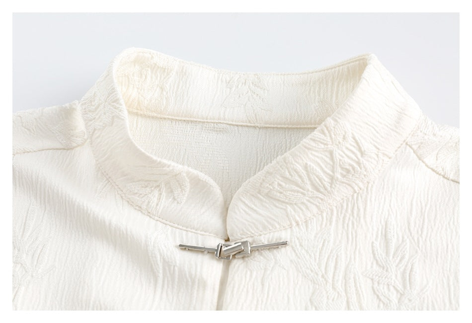 Close-up of an ivory shirt's floral-textured collar and silver metal clasp.
