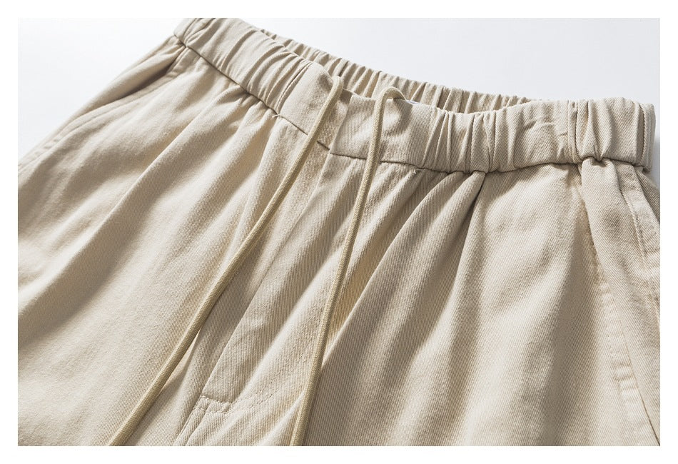 Close-up of beige pants with a gathered elastic waistband, front drawstring, and pocket seam.