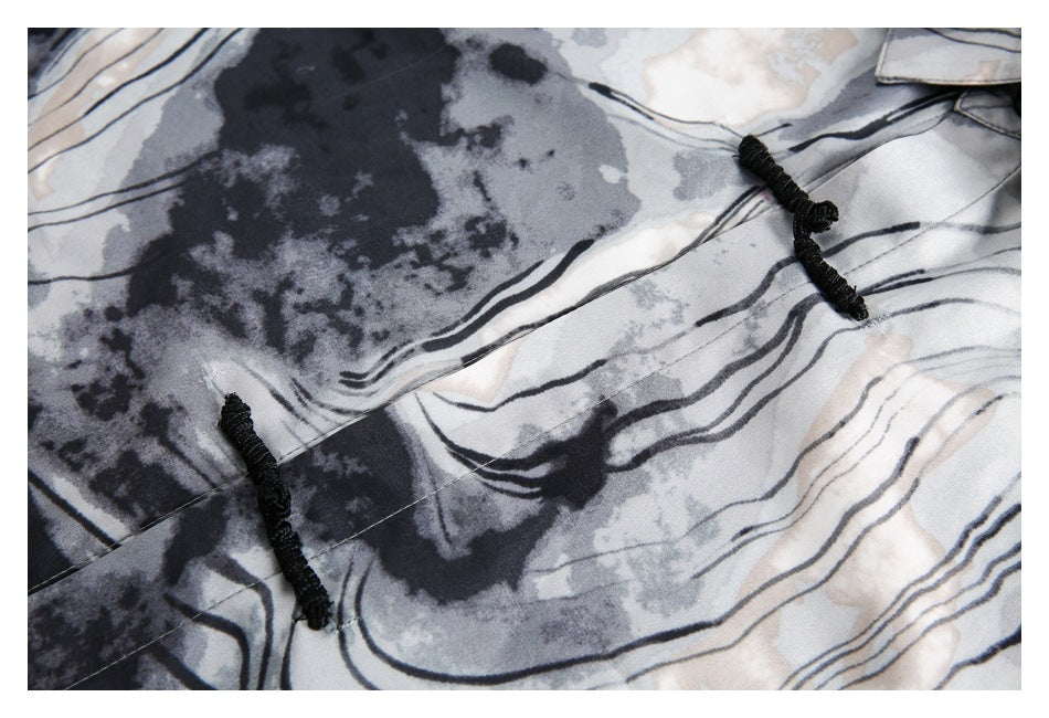 Close-up of two black knotted frog closures on a gray, black, and cream abstract-print shirt.