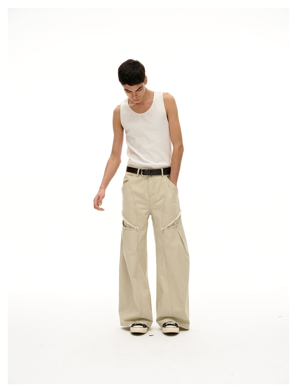 Model wearing oversized light beige wide-leg pants with layered knee panels and a white tank top, front view.