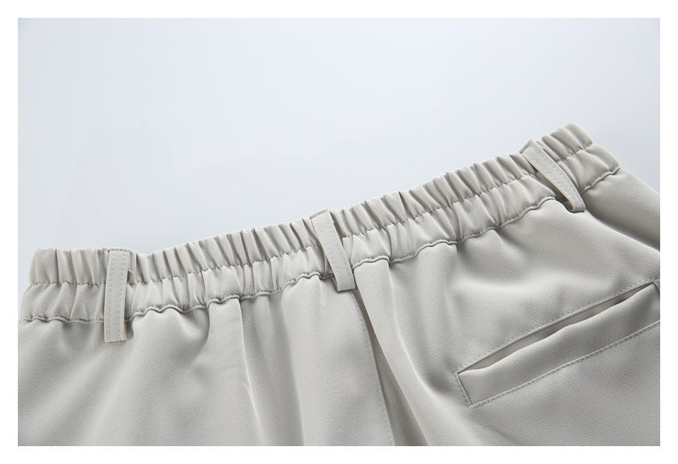 Close-up of the elasticated back waistband, belt loops and welt pocket on light beige trousers.
