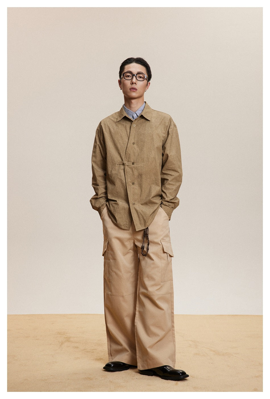 Full-length model wearing a tan button-front shirt jacket with a waist tab and beige cargo pants.