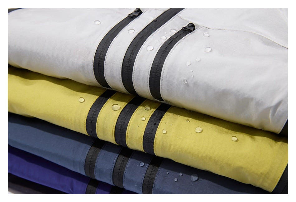 Close-up of folded white, yellow, gray, and blue jacket fabric with black zippers and water droplets.