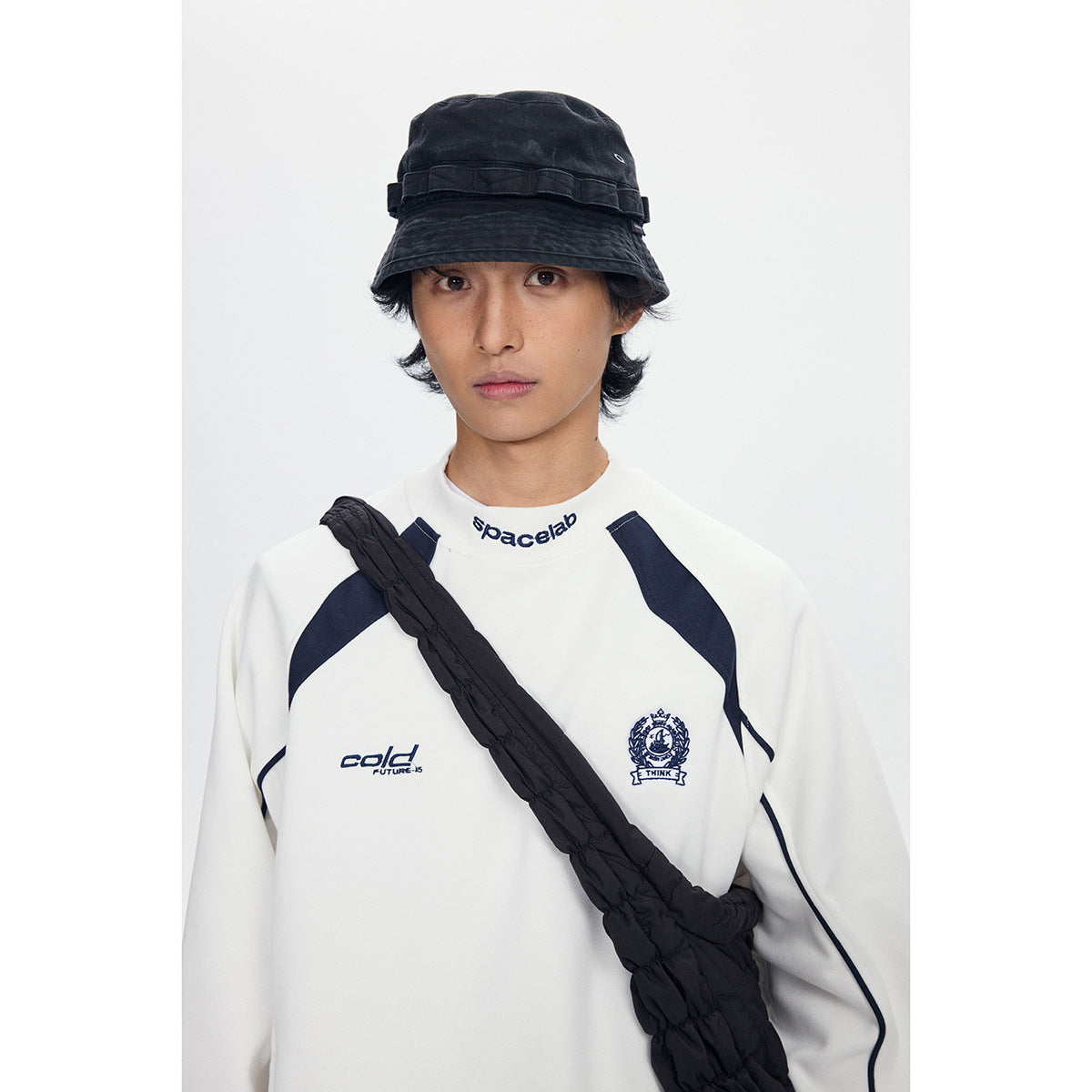 Close view of a model wearing a white sweatshirt with navy accents and a black bucket hat.