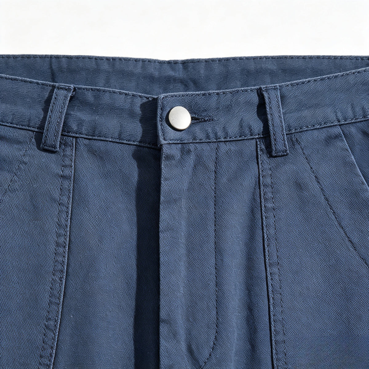 Close-up of blue trousers showing the waistband, belt loops, silver button, and front pleats.