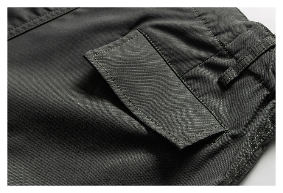 Close-up of charcoal trousers showing a rectangular flap pocket, belt loop, and stitched seams.