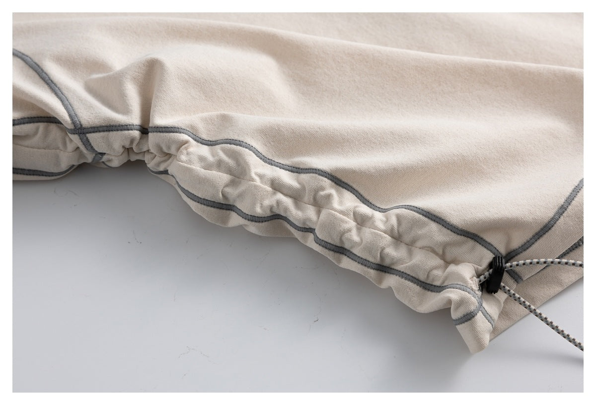 Close-up of a beige garment's gathered drawcord edge, with gray seam detailing and a black cord lock.