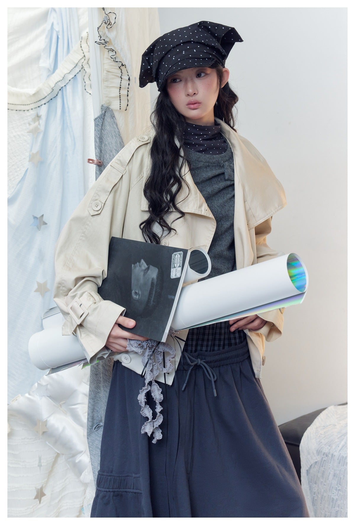Model wearing a cream oversized jacket over a gray top and navy bottoms, with a black polka-dot headscarf.