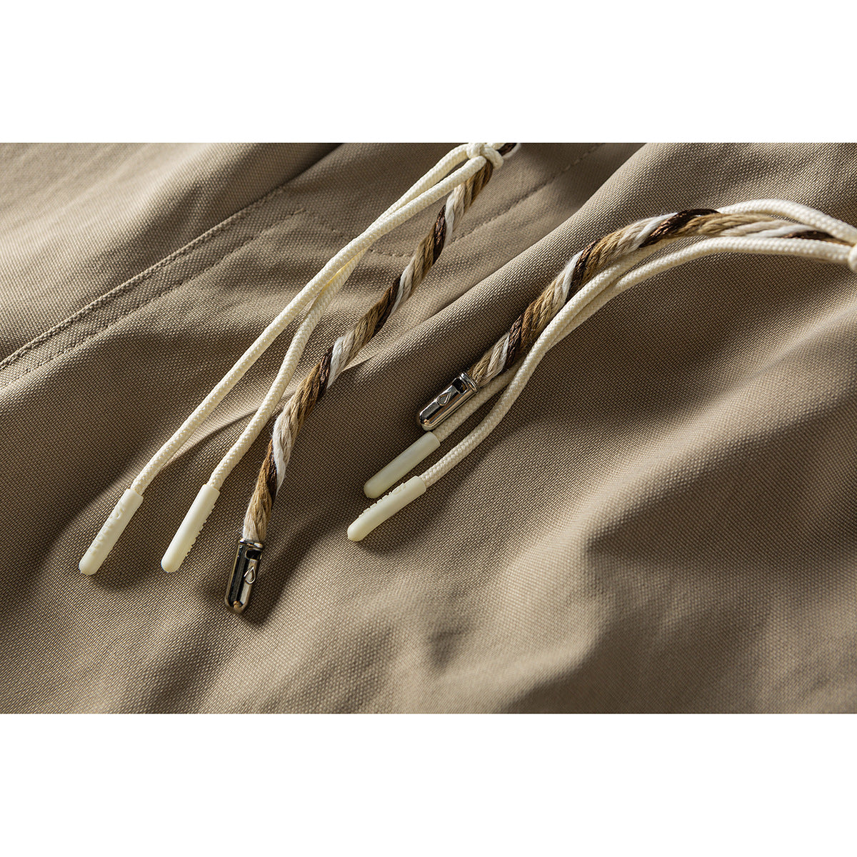Close-up of taupe trousers with cream and brown braided drawstrings and metal cord ends.