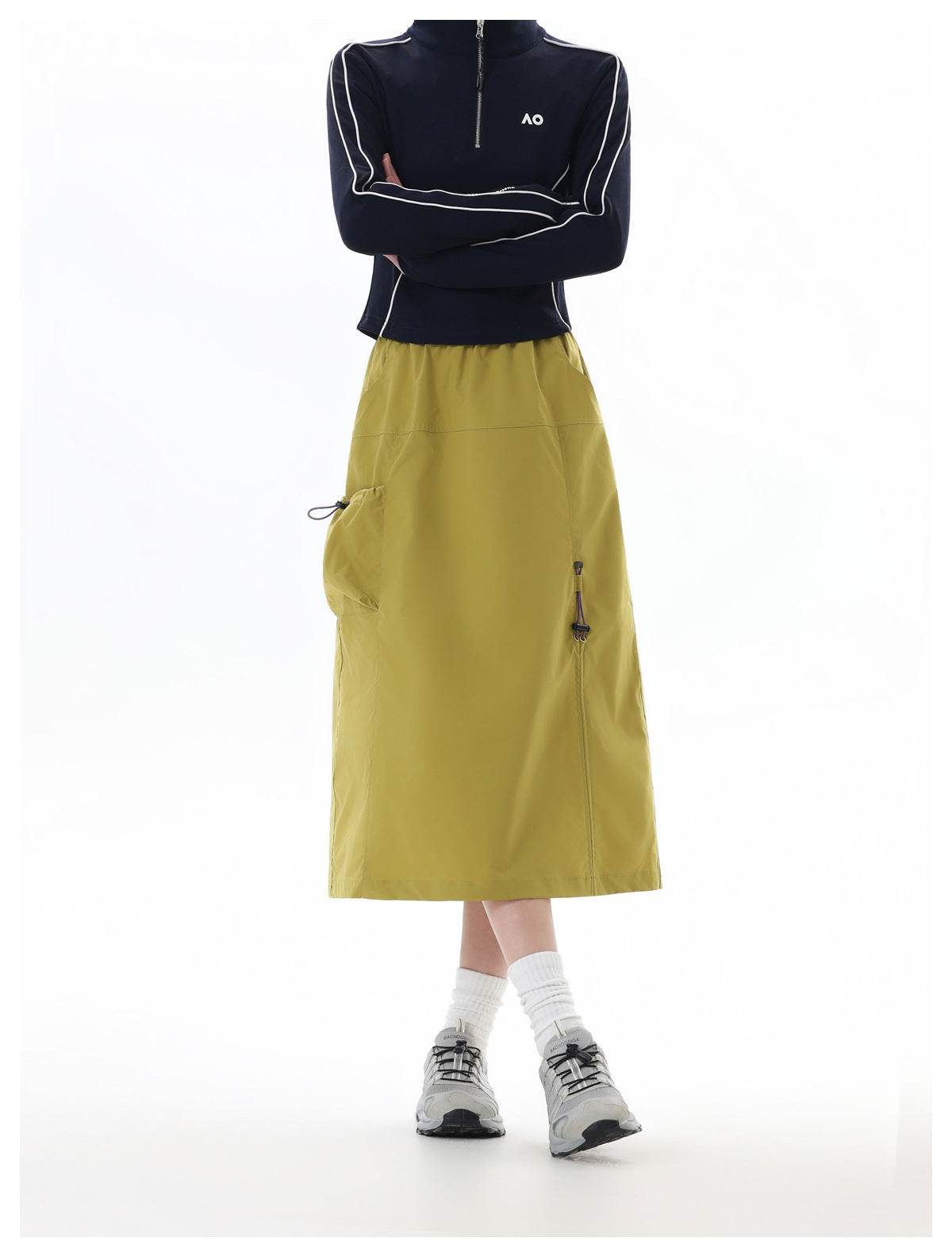 Front view of a model wearing a mustard-olive midi skirt with a side pocket and a navy top with white piping.
