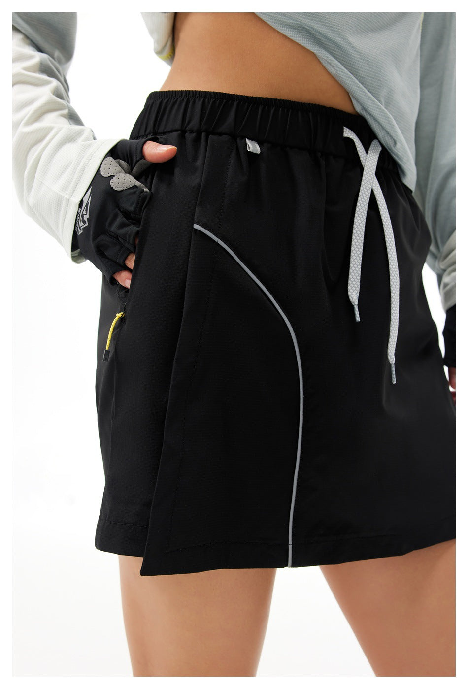 Close-up of a black athletic skort with an elastic drawstring waist, curved gray piping, and a zip pocket.