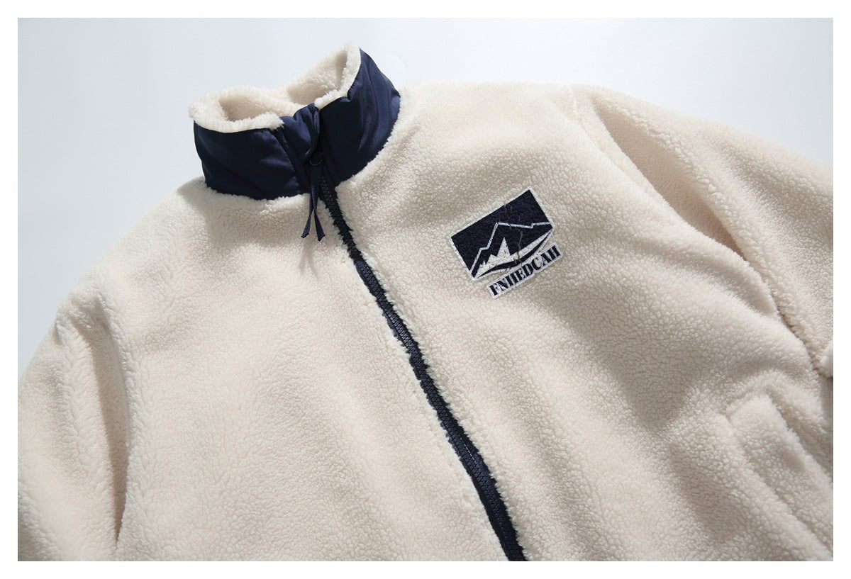 Close front view of an ivory fleece jacket with a navy stand collar, zipper, and chest patch.