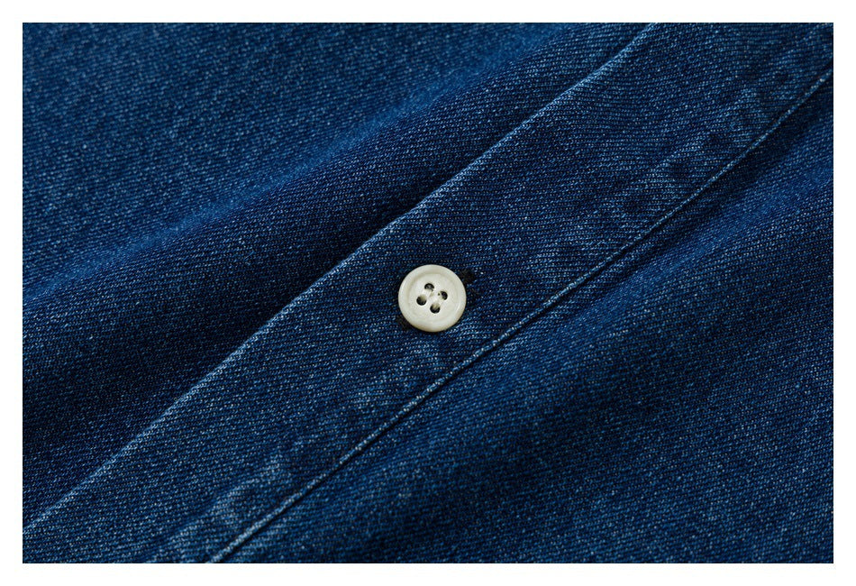 Close-up of a cream button and stitched placket on dark blue denim.