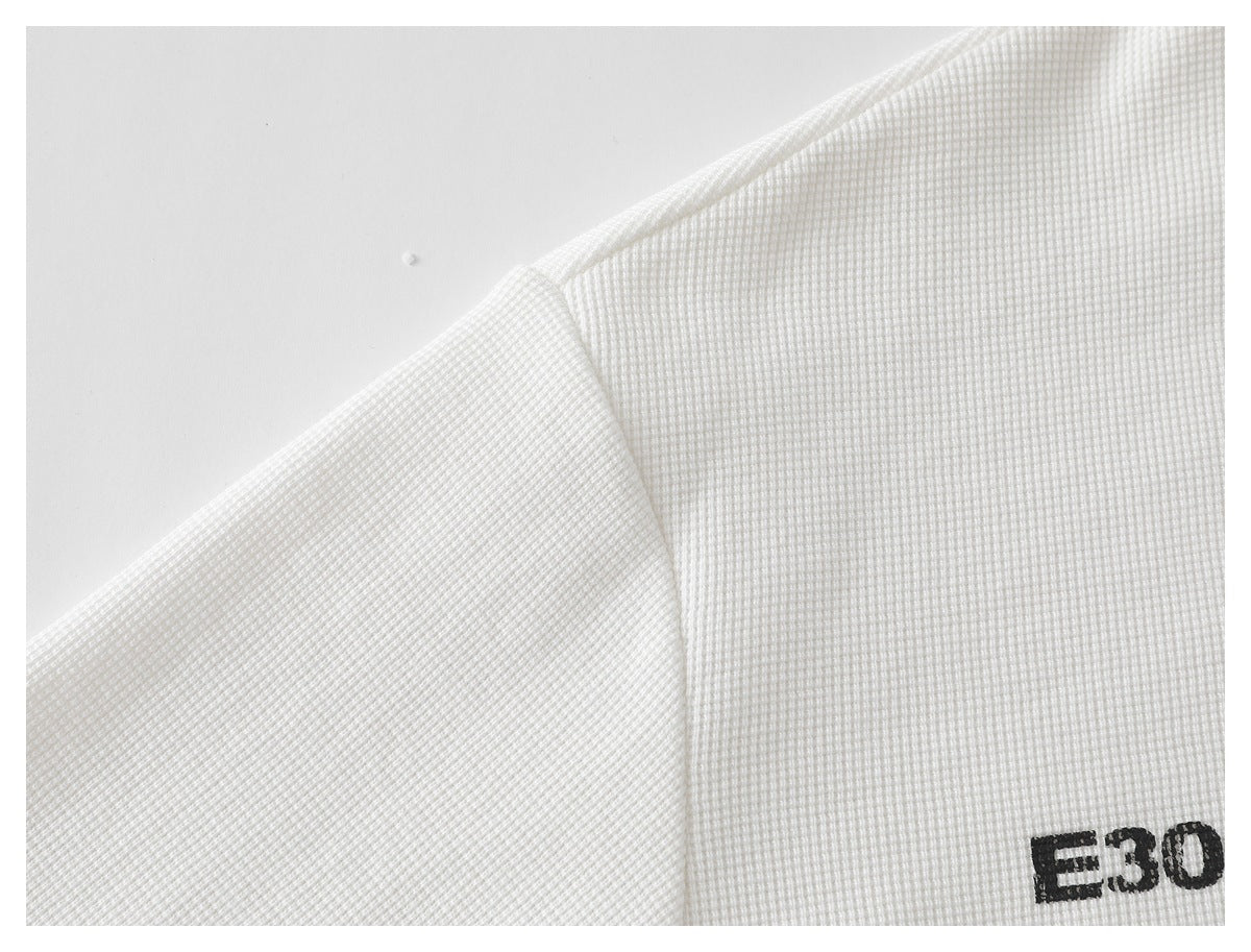 Close-up of a white waffle-knit shirt's shoulder seam and partial black lettering near the edge.