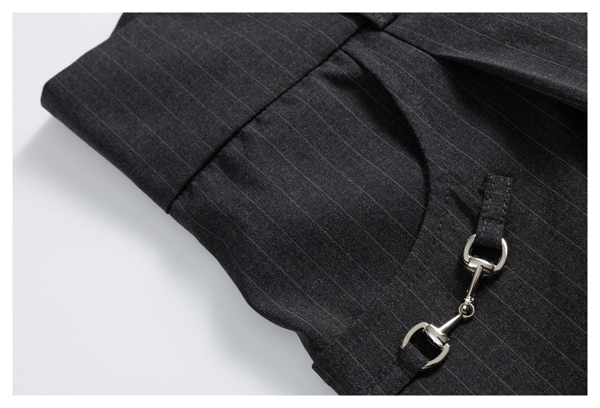 Close-up of charcoal pinstripe trousers showing a curved pocket opening and silver hook-and-eye hardware.