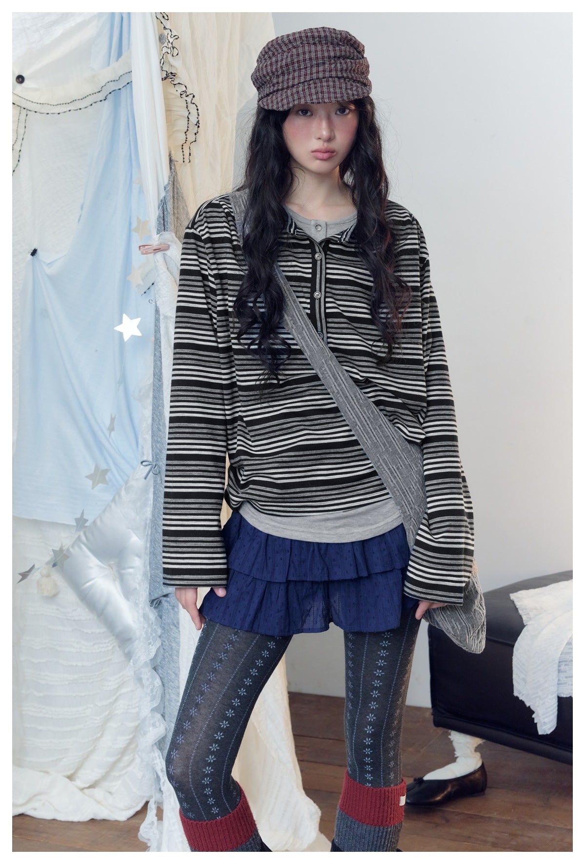 Model wearing a black and gray striped henley over a gray top, with a navy ruffled skirt and patterned tights.