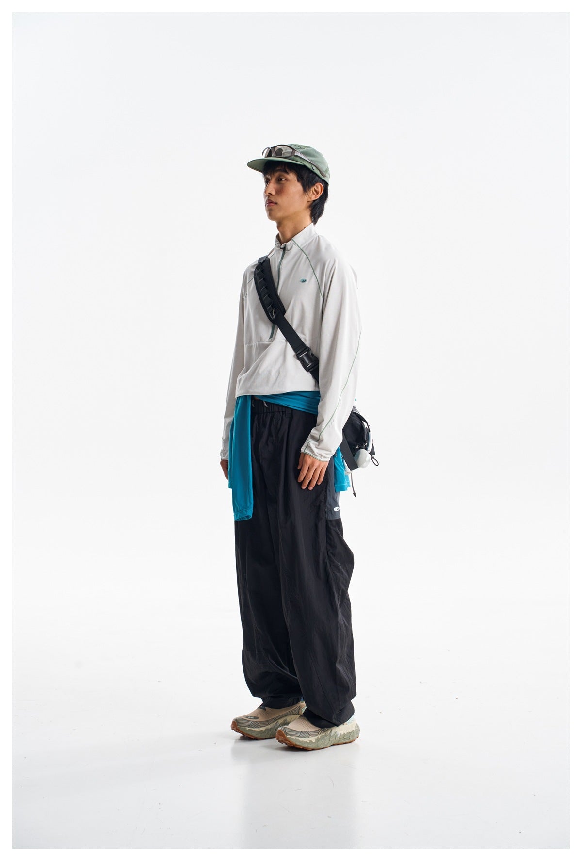 Model wearing a light gray long-sleeve quarter-zip top, loose black pants, and a turquoise layer tied at the waist.
