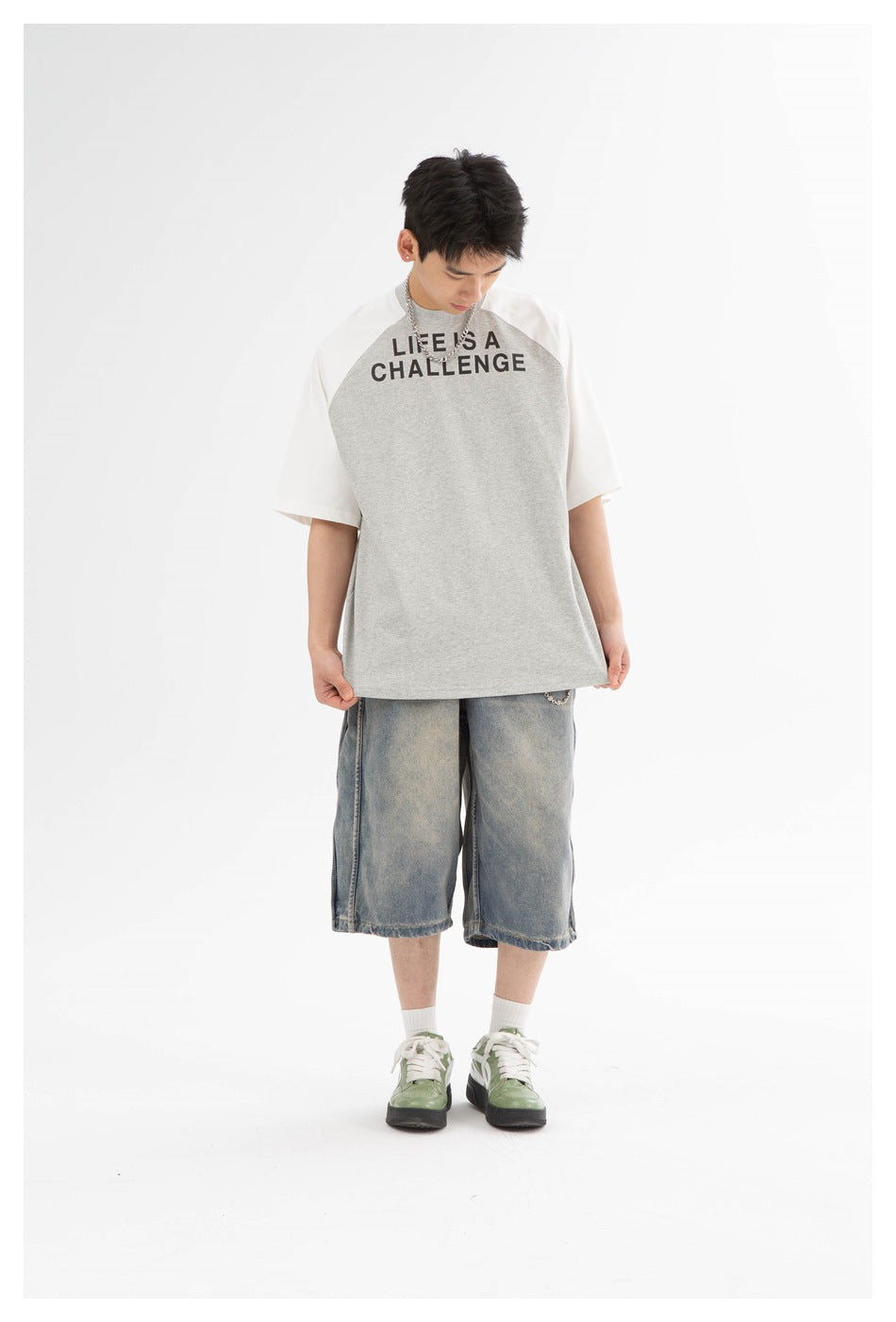 Front view of a model wearing a gray-and-white raglan T-shirt with black “LIFE IS A CHALLENGE” text and denim shorts.