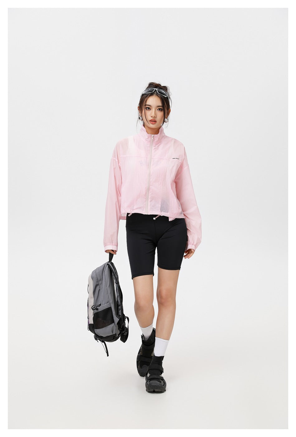 Full-length view of a model wearing a light pink zip-front jacket with a stand collar and black cycling shorts.