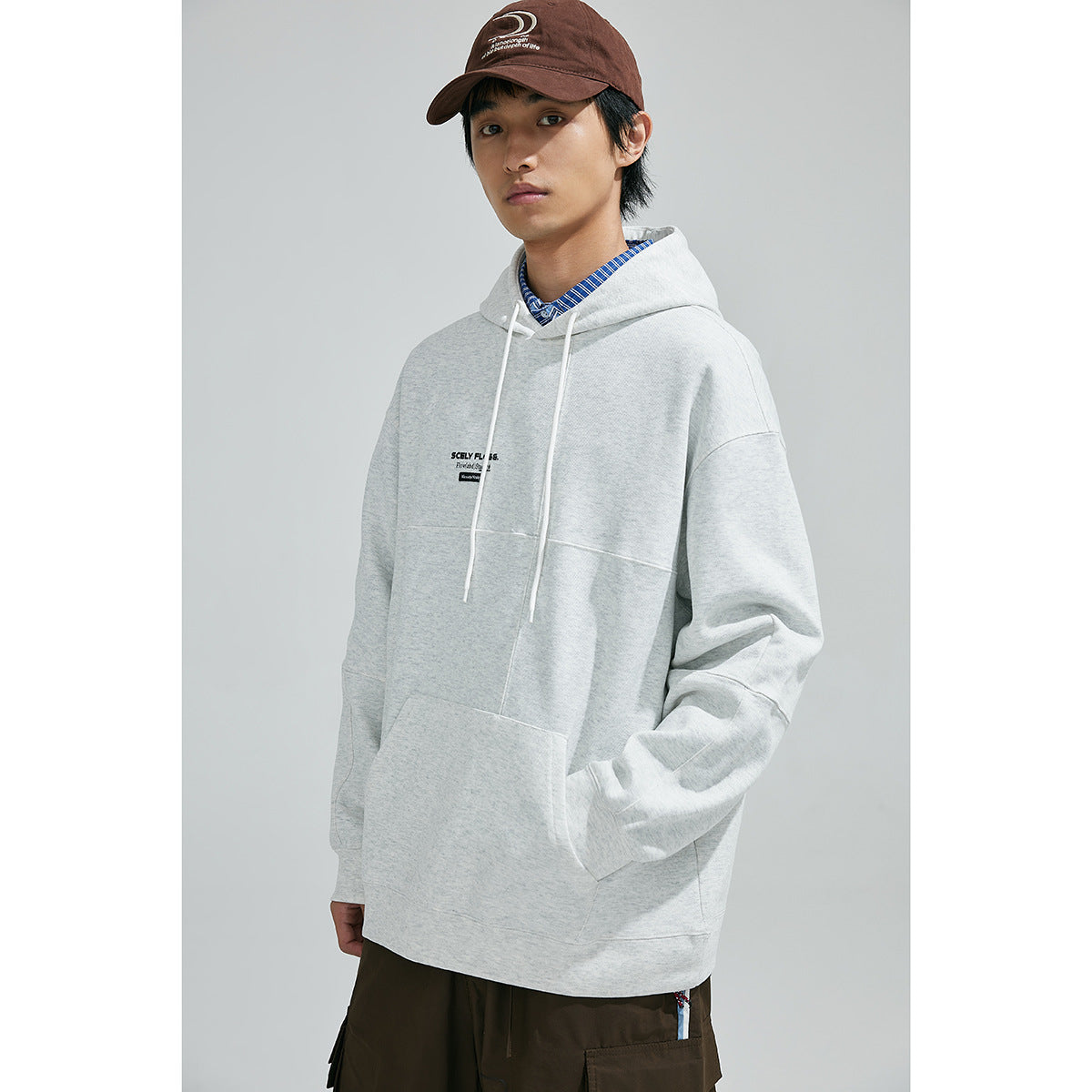 Model wearing a light gray hooded sweatshirt with drawstrings and kangaroo pocket, shown from the front.