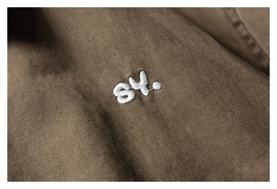 Close-up of small white embroidered lettering on brown jacket fabric.
