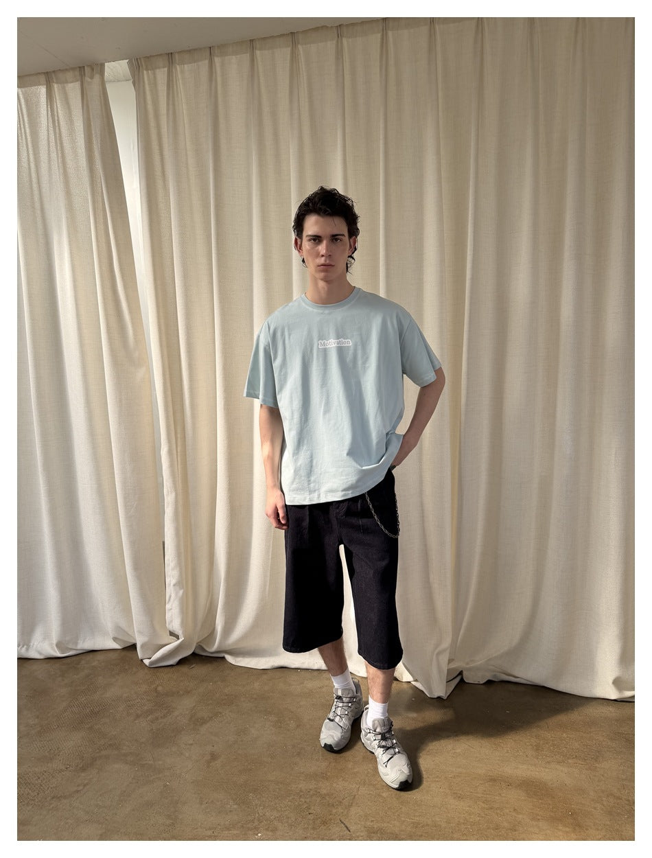 Full-length model wearing a pale blue T-shirt with a small chest print and black shorts.