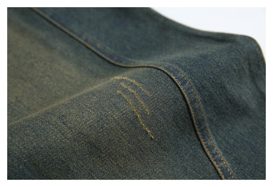 Close-up of dark denim with a curved orange-stitched seam and small distressed marks.
