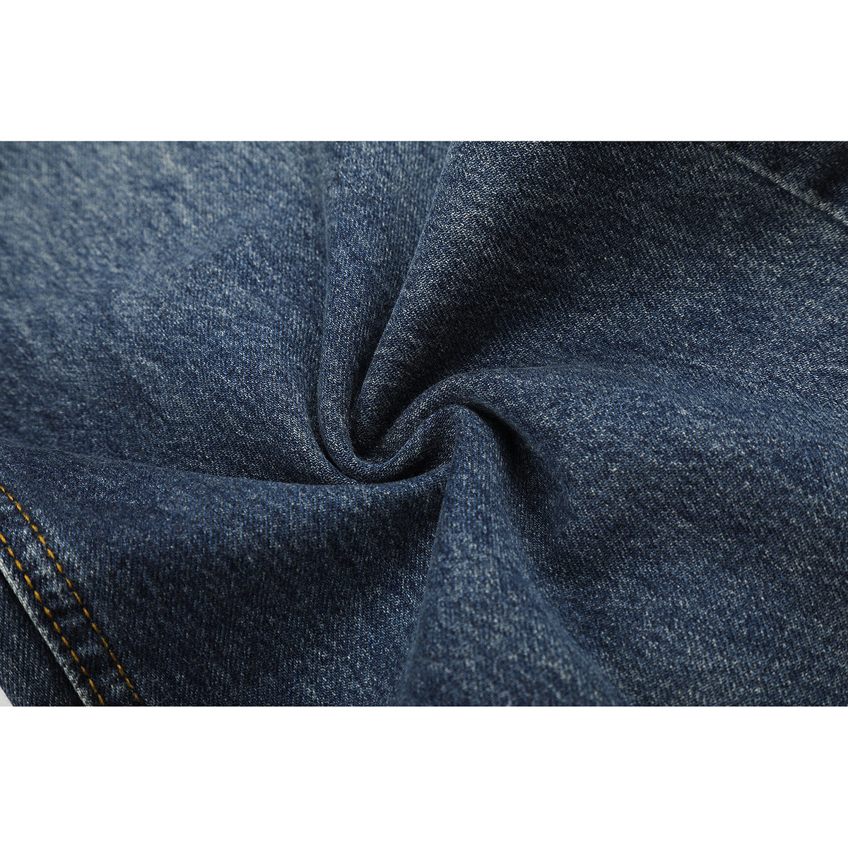Macro view of dark blue denim gathered into a fold, showing its woven texture and a stitched edge.
