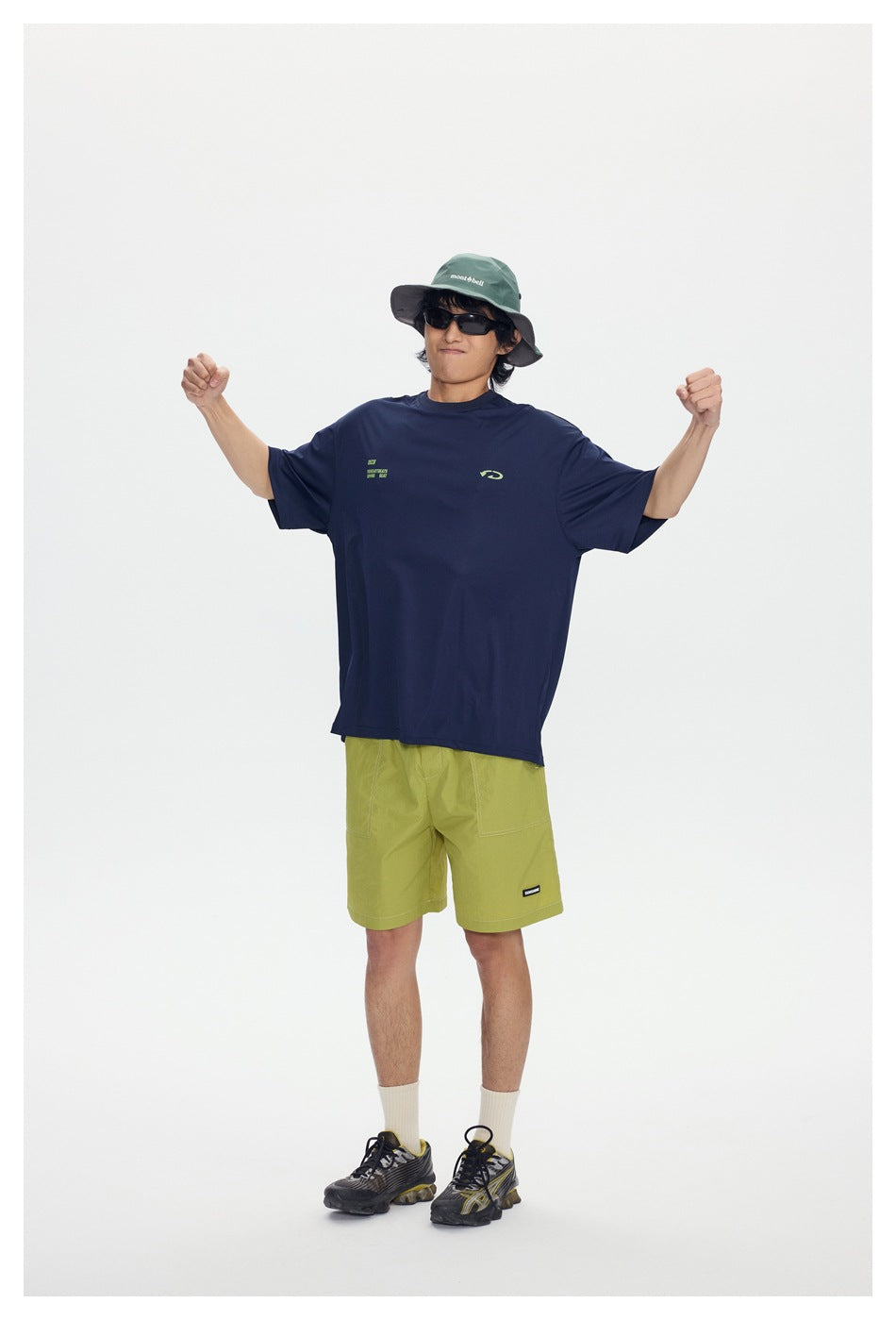 Model in a navy T-shirt with lime chest graphics and lime shorts, raising both arms.