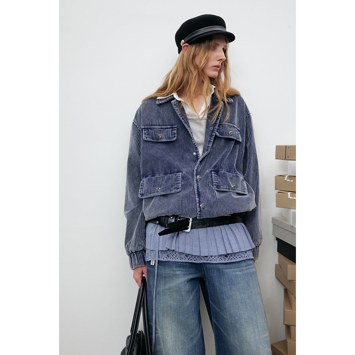 Model in a blue ribbed jacket with four buttoned flap pockets, layered over a light top and pleated skirt.