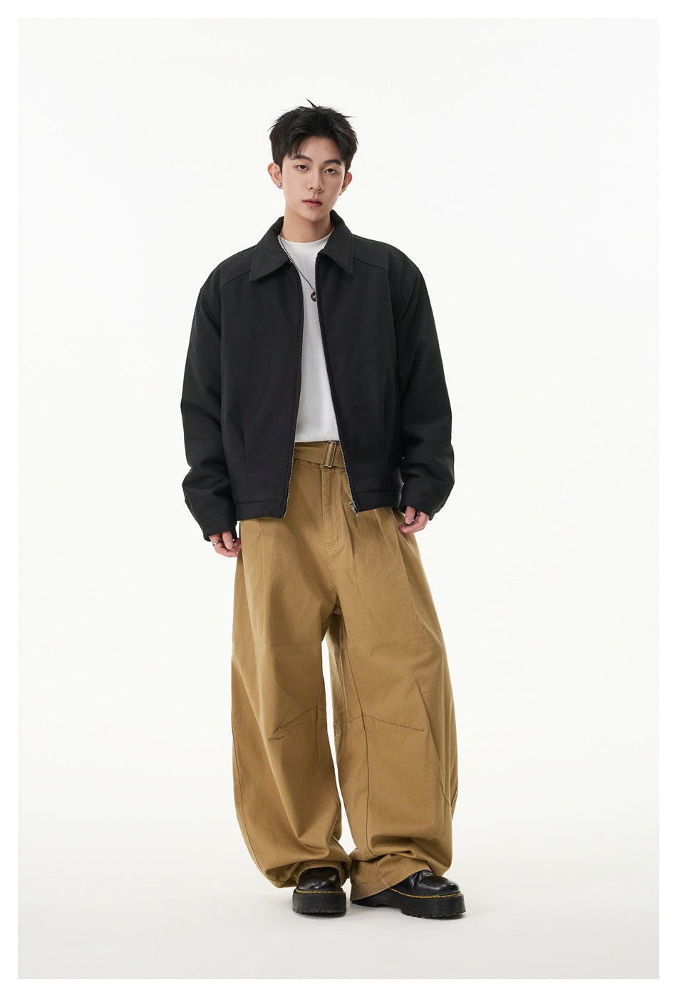 Model wearing black zip-up collared jacket over a white tee with wide tan pants and black boots