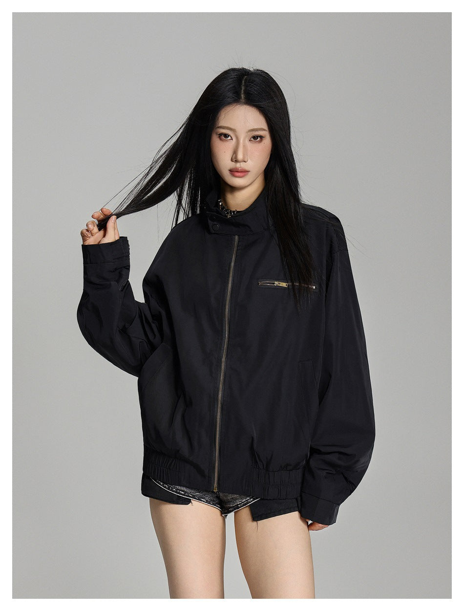 Front view of a model in a black oversized jacket with a stand collar, gold-tone zippers and gathered hem.