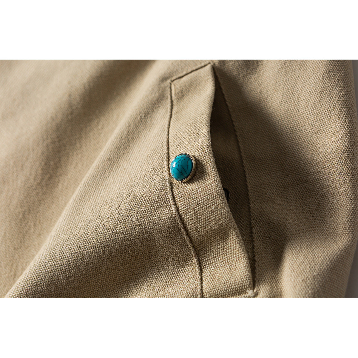 Close-up of a turquoise button on a beige garment flap, with visible stitching and textured fabric.