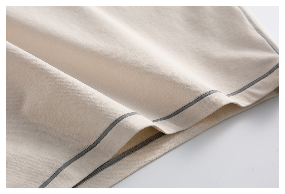 Close-up of a beige garment hem with curved dark gray stitching and a folded edge.