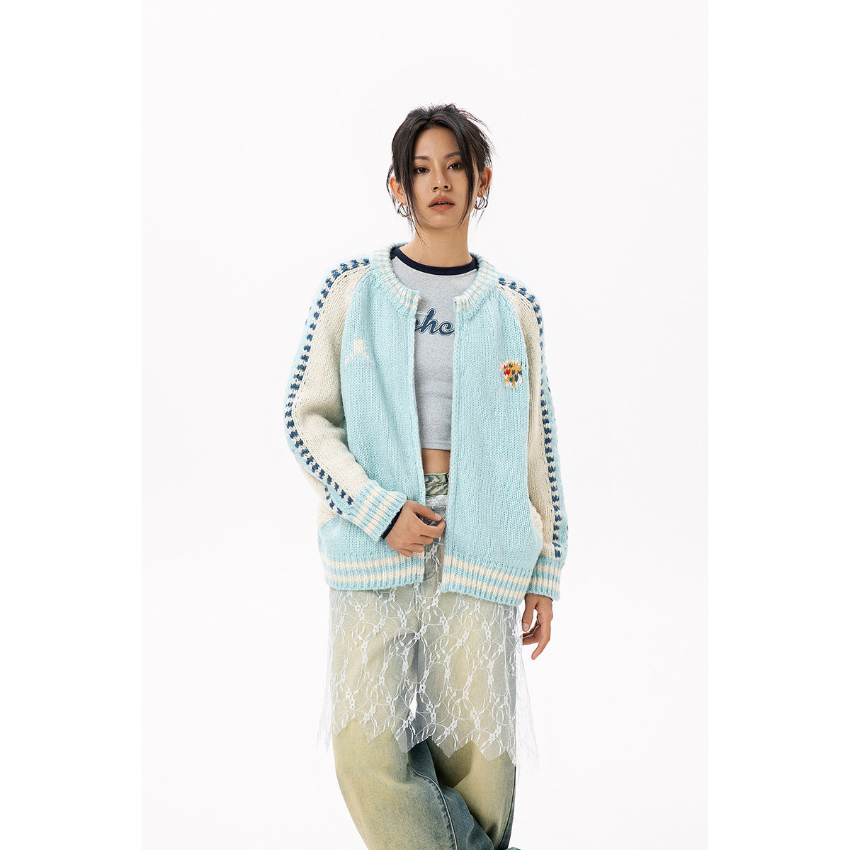 Model wearing an open pale blue cardigan with cream sleeves and blue stripe details, styled over a top and jeans.