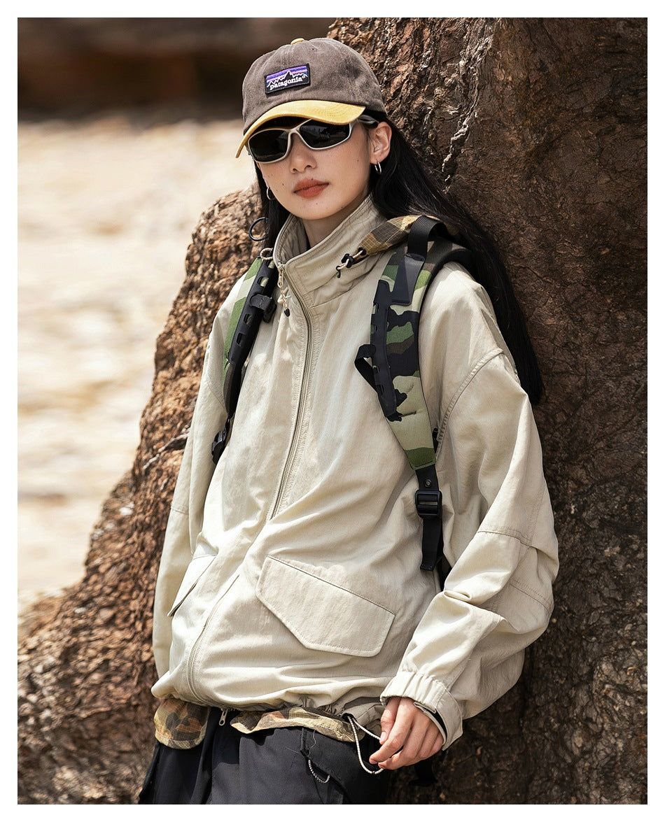 A woman models a cream oversized zip jacket with a high collar, large front pocket and elastic cuffs outdoors.