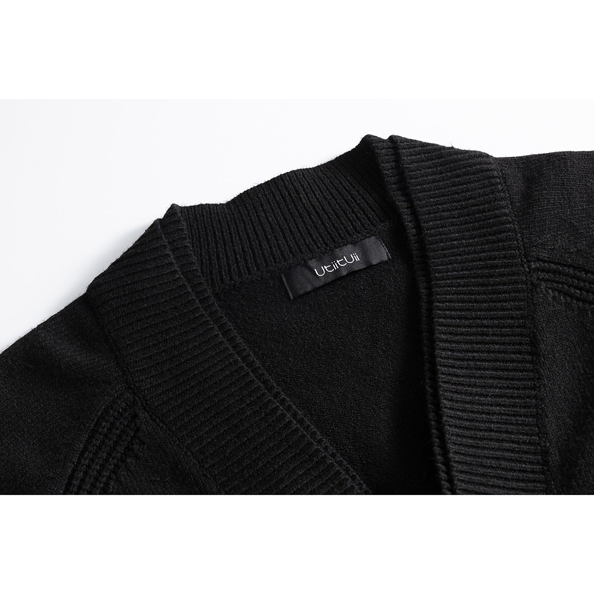 Close-up of a black knit cardigan’s ribbed shawl collar and inner neck label.