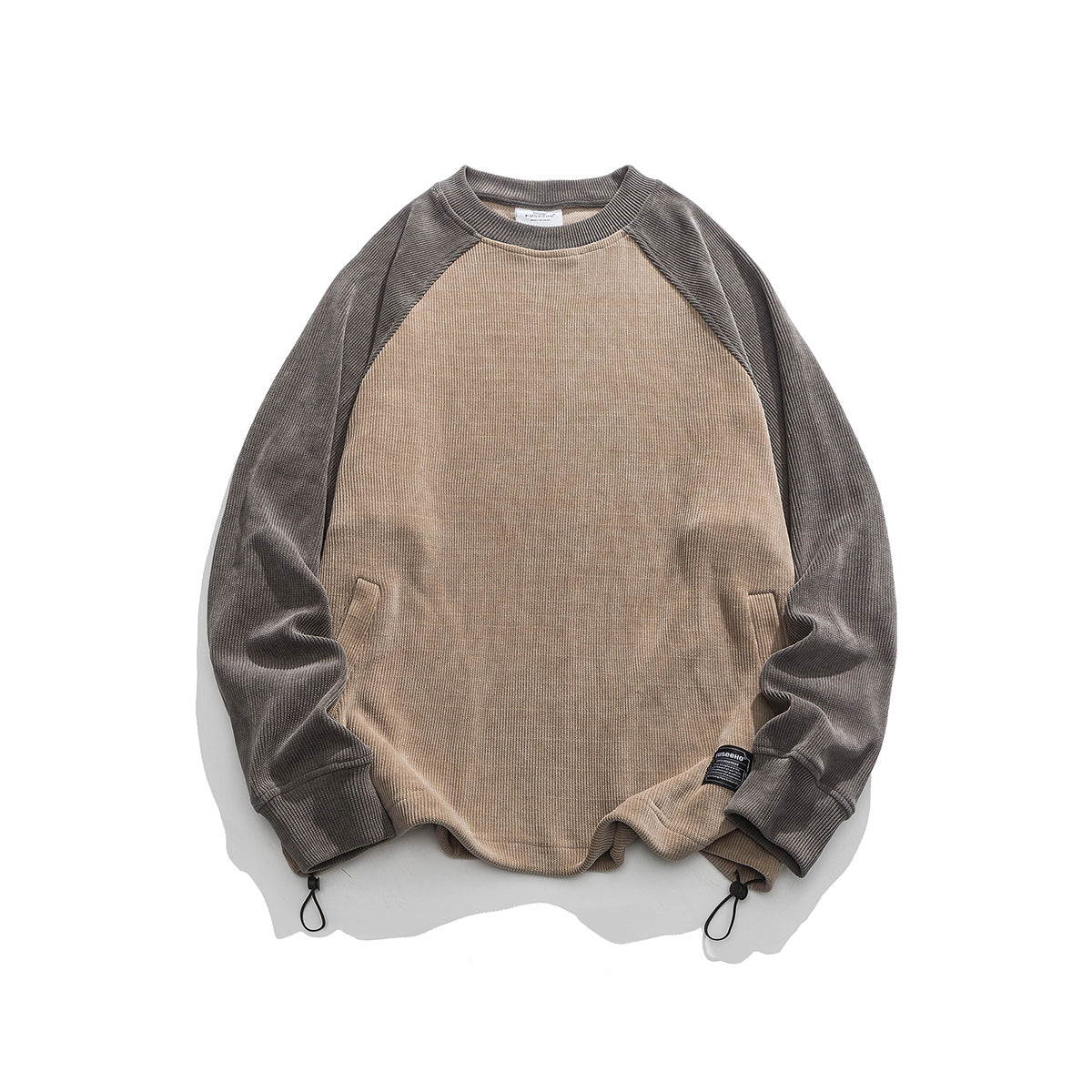 Tan ribbed crewneck sweatshirt with brown-gray raglan sleeves, slanted pockets and hem drawcord toggles, flat lay