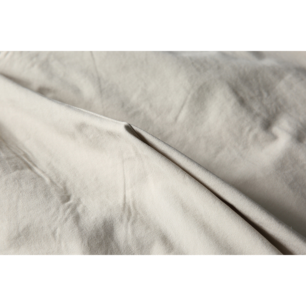 Close-up of light beige fabric draped in folds, showing its subtle surface texture.