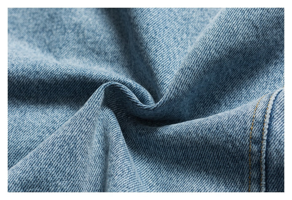 Close-up of light blue denim fabric gathered into folds, showing its woven texture and stitching.