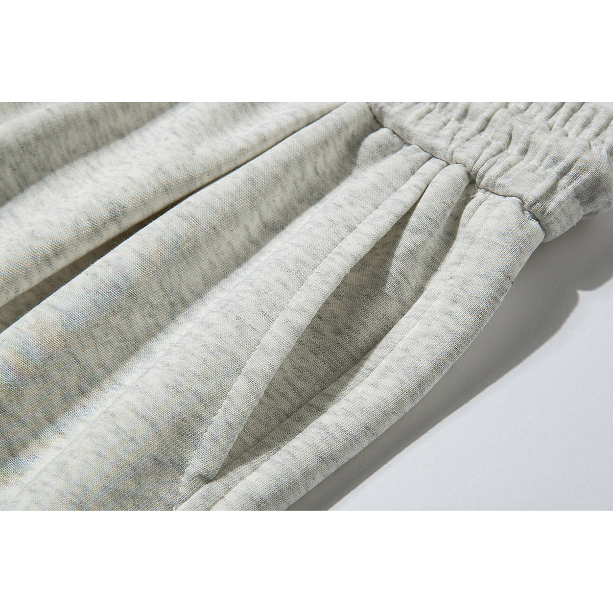 Close-up of the gathered elastic waistband and fabric drawstrings on light gray pants.