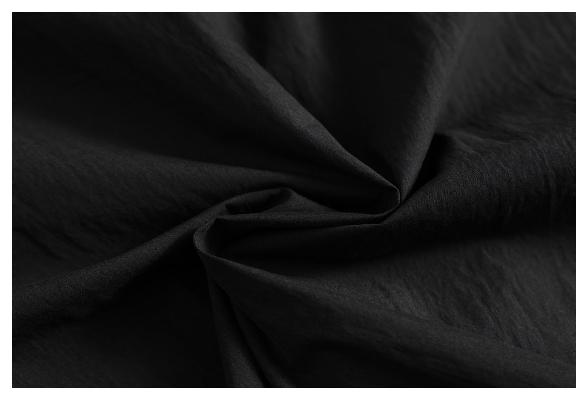 Close-up of black fabric draped into soft folds, showing its subtle texture.