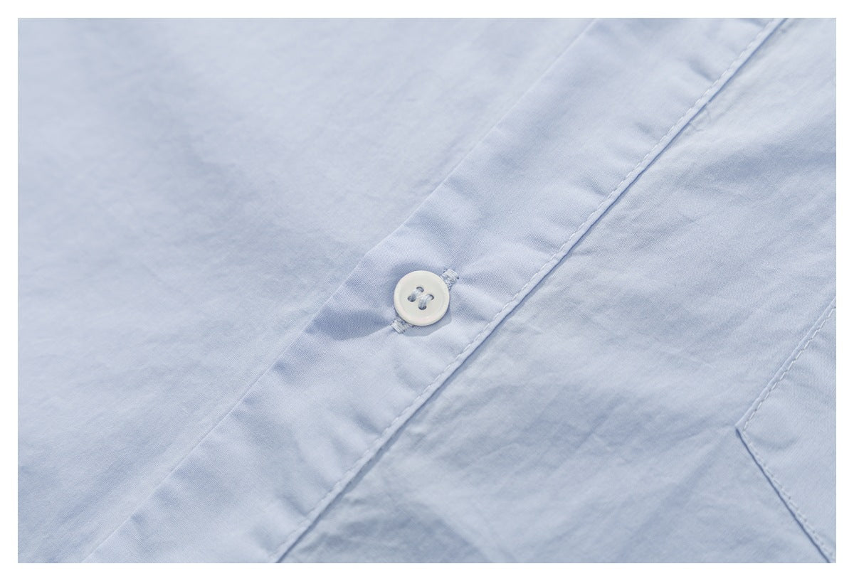 Close-up of a white button and stitched placket on pale blue shirt fabric.
