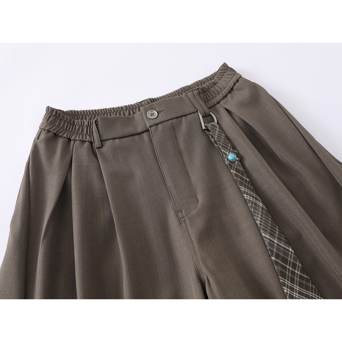 Close-up of taupe shorts showing an elastic waistband, front pleats, button, and plaid hanging strap with a turquoise accent.