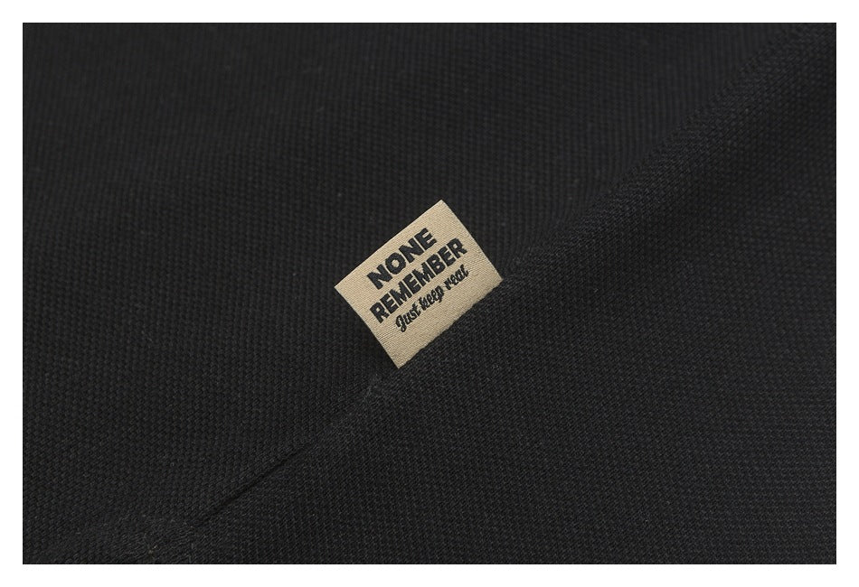 Close-up of black polo fabric with a small beige label reading “NONE REMEMBER” and “Just keep moving.”